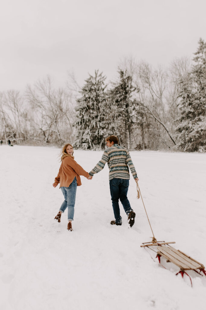 Iowa Wedding Photographer, couple walks up the hill in the snow in December, girl looks back at the camera