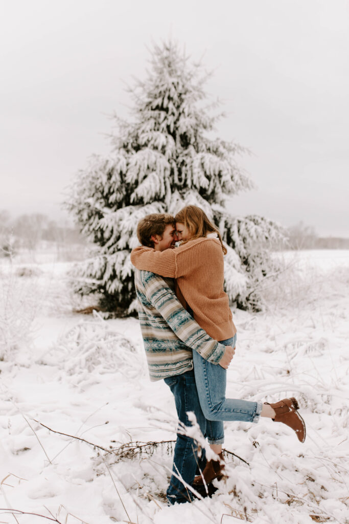 Iowa snowy engagement photos, groom picks up bride and kisses her in front of snow covered tree