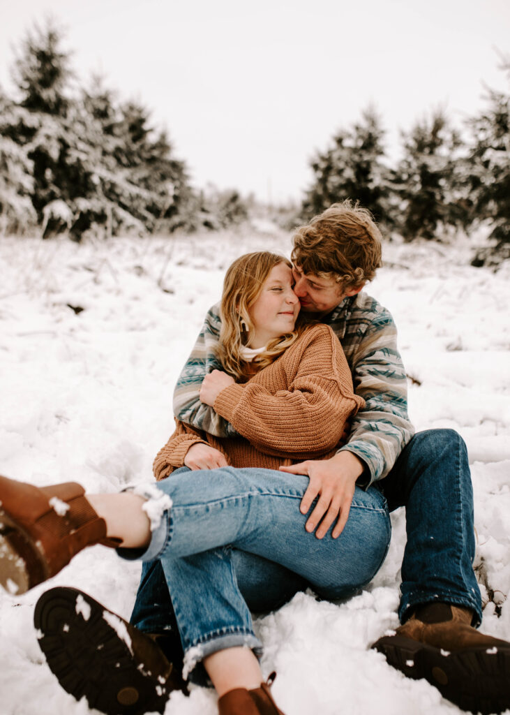 couple sits in the snow together snuggled together