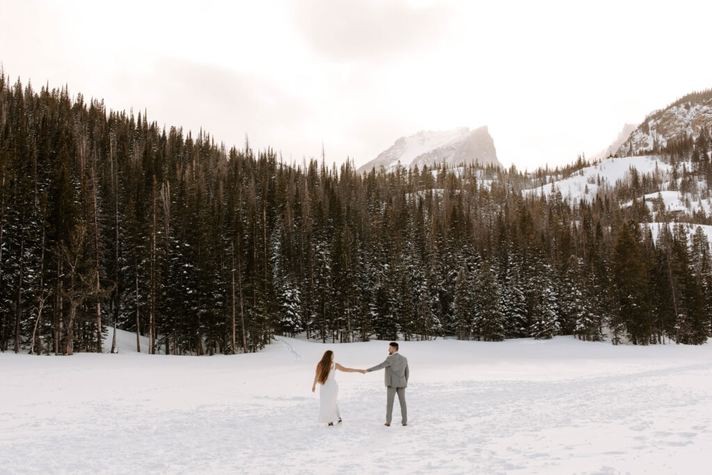 couple holds hands and walks on frozen lake in rmnp