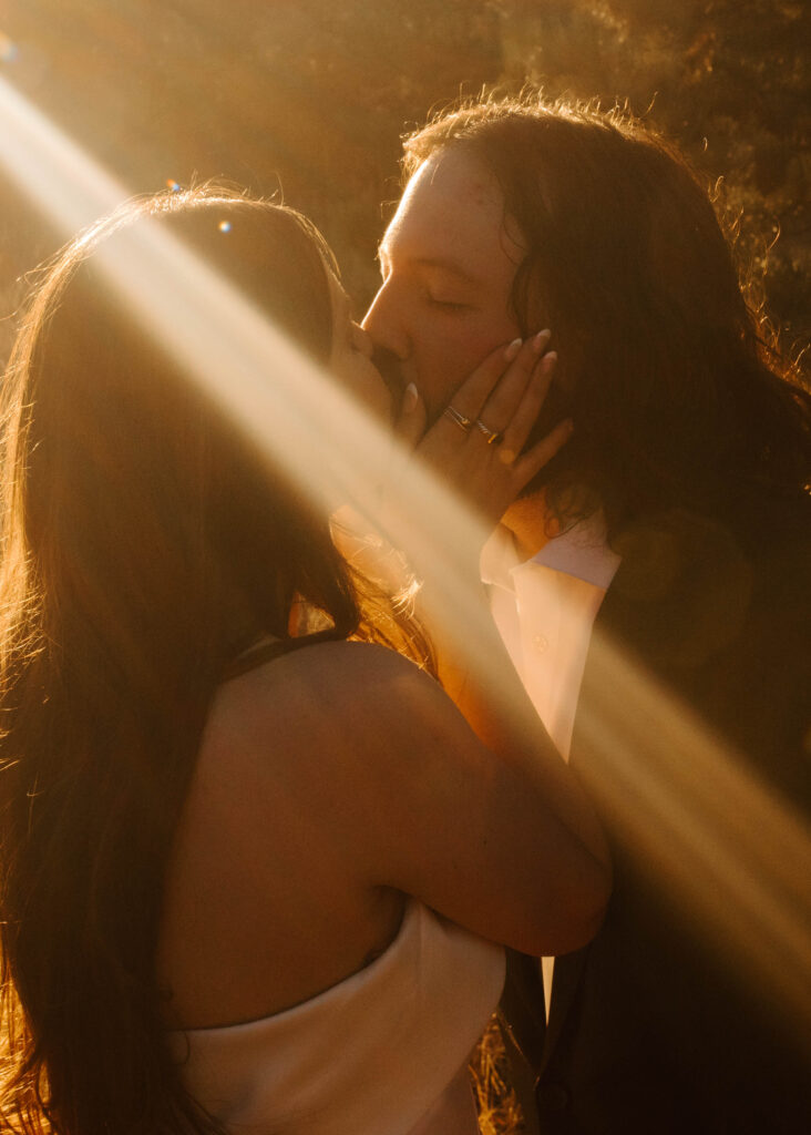 bride and groom kiss as golden light streams onto their faces