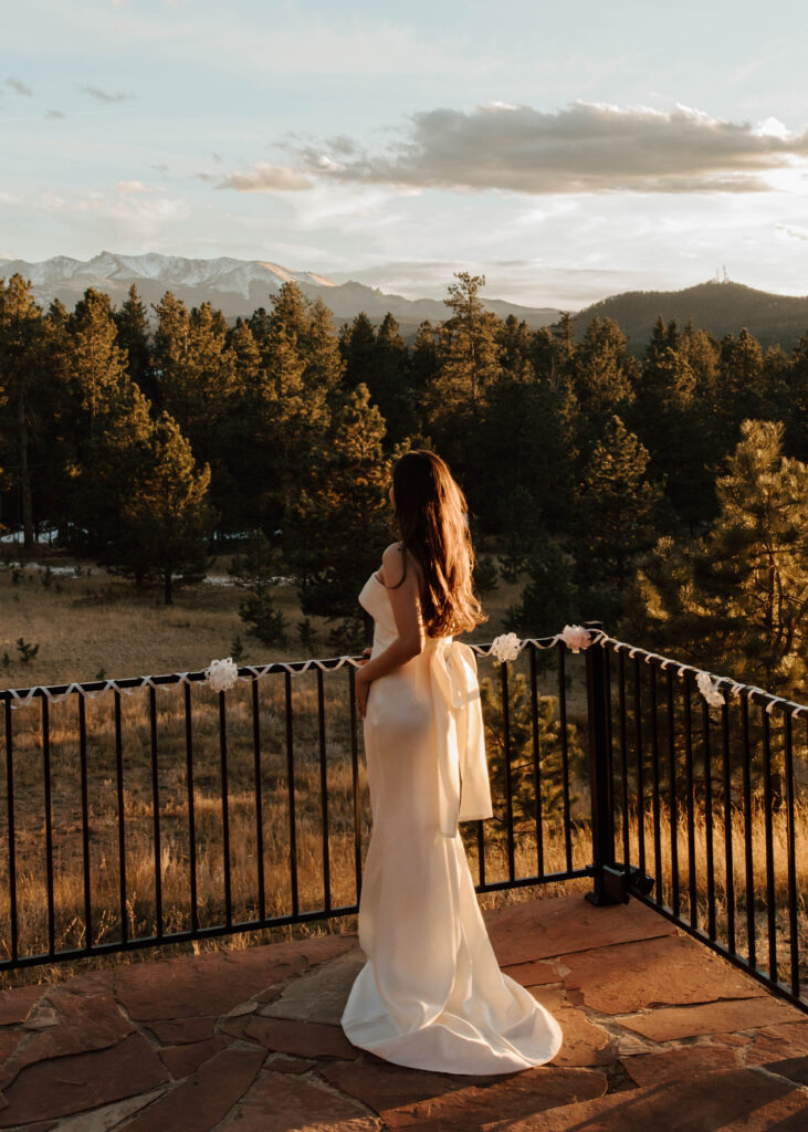 bride wears bow on her dress and looks to the sunset over the mountains 