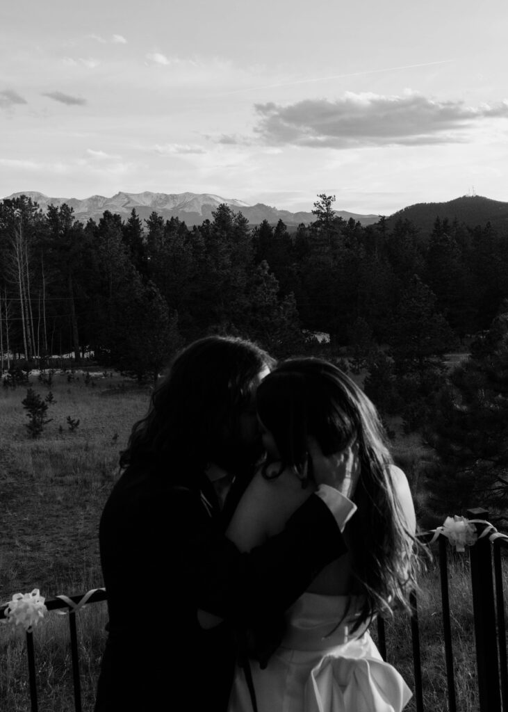 couple kisses as sun sets over mountains on their wedding day
