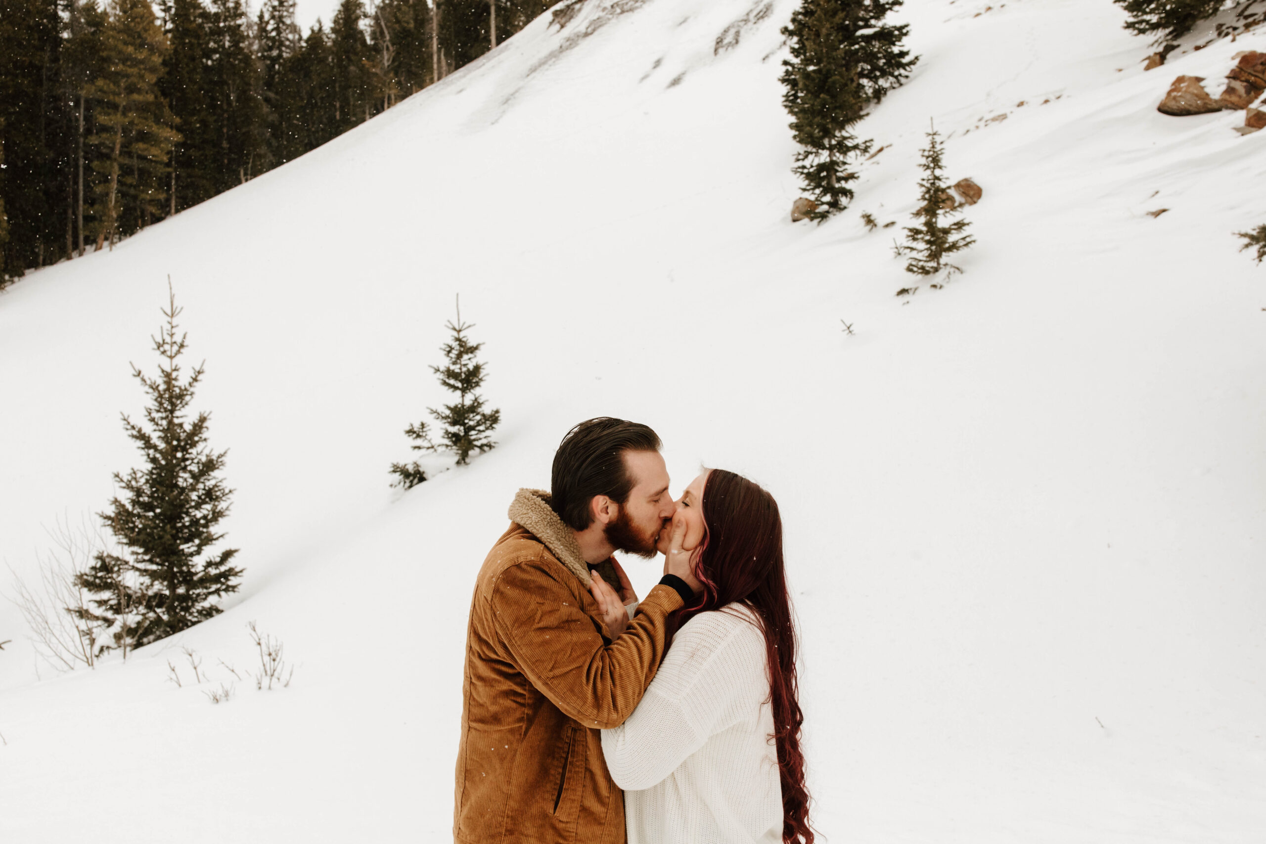 he grabs his fiancé's face and kisses her. they are surrounded by a mountain of snow
