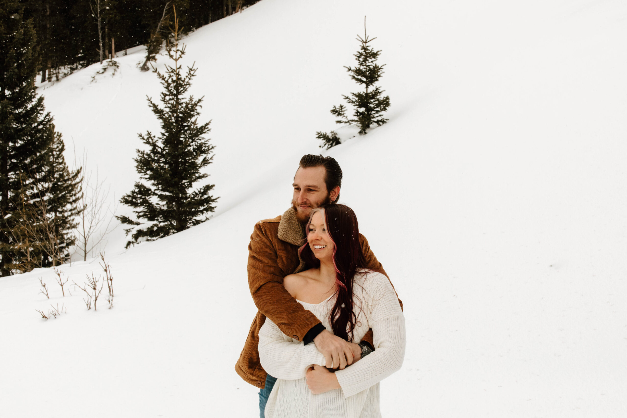 he hugs her from behind, they look off at the snow covered mountains in Breckenridge
