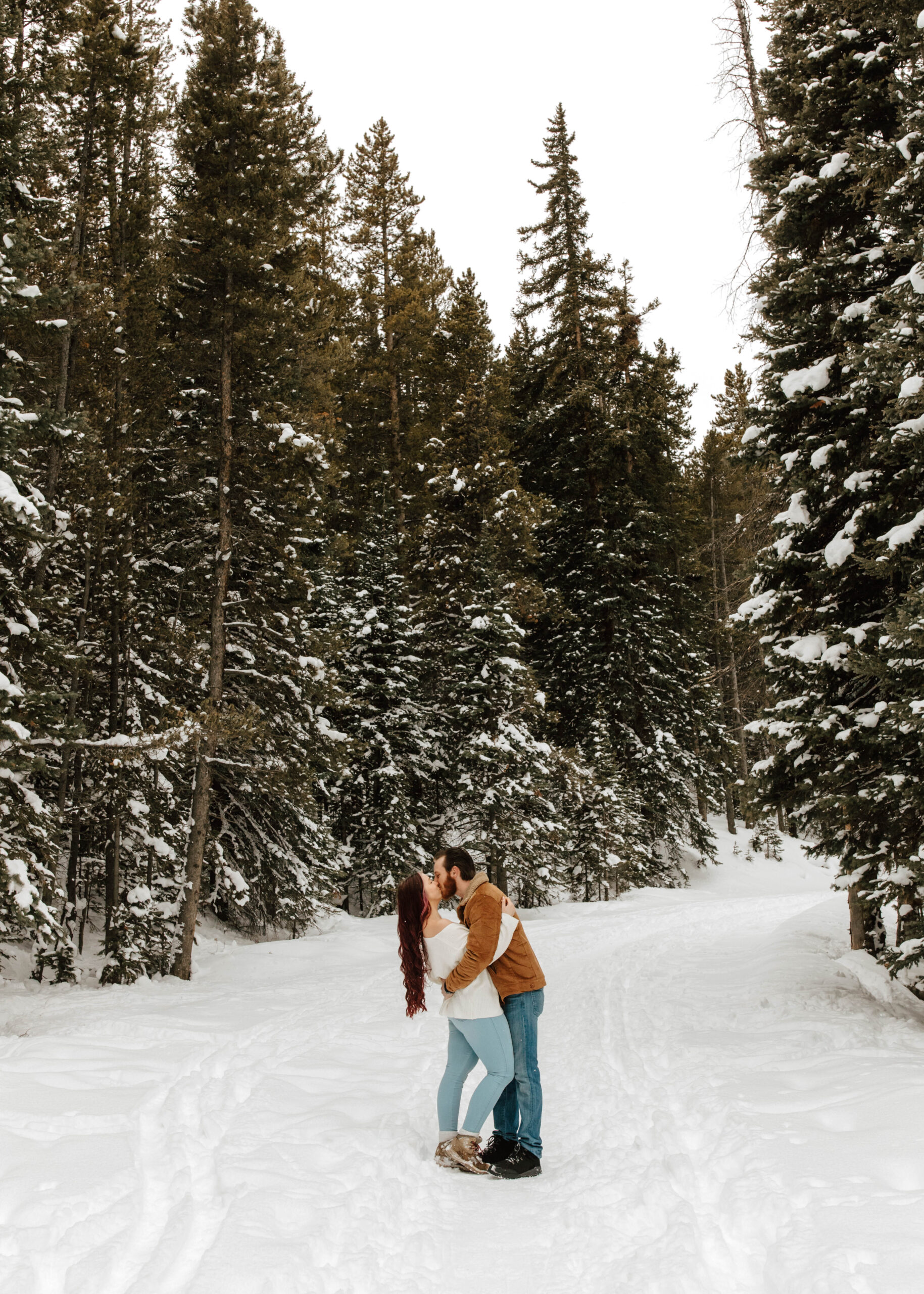 couple kisses while surrounded by tall evergreen trees in the snow in Breckenridge, CO