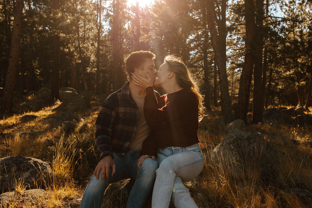 couple sits on a rock and kisses in the trees