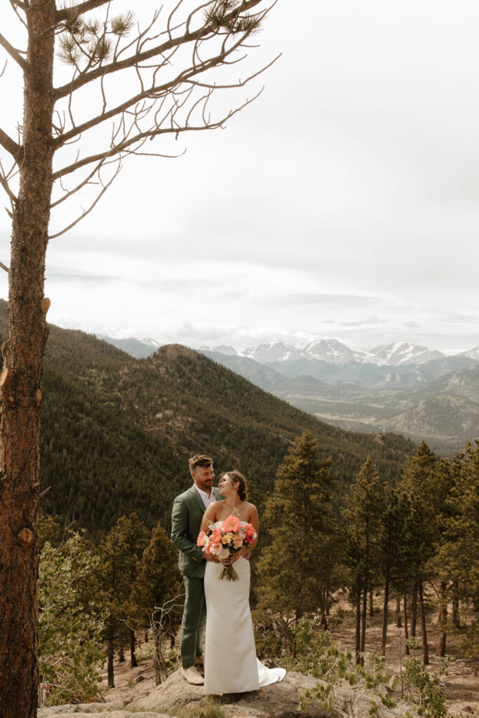 bride and groom stand on cliff in mountains