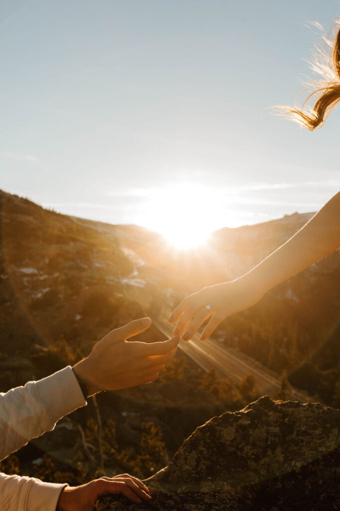 engagement ring on her hand as her hair blows in the wind, hands reaching to each other