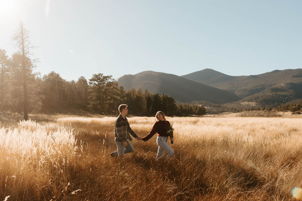 holding hands walking through the meadow smiling at each other