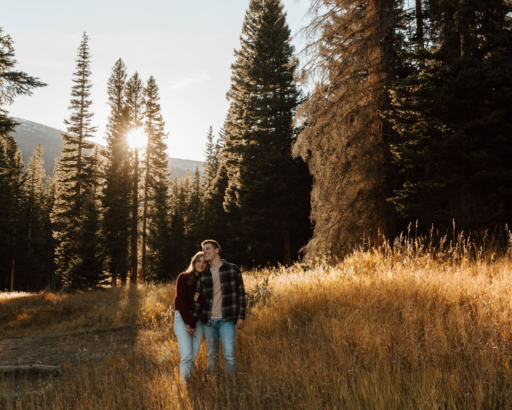 couple snuggling together between the tall trees in the meadow