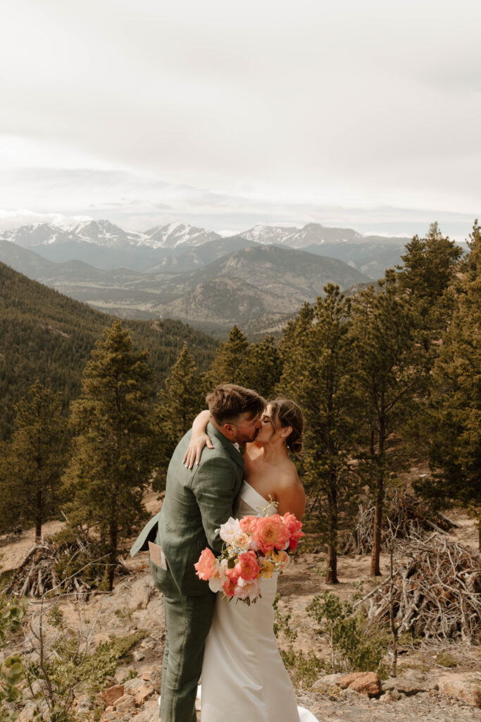 bride and groom kiss in front of mountain backdrop