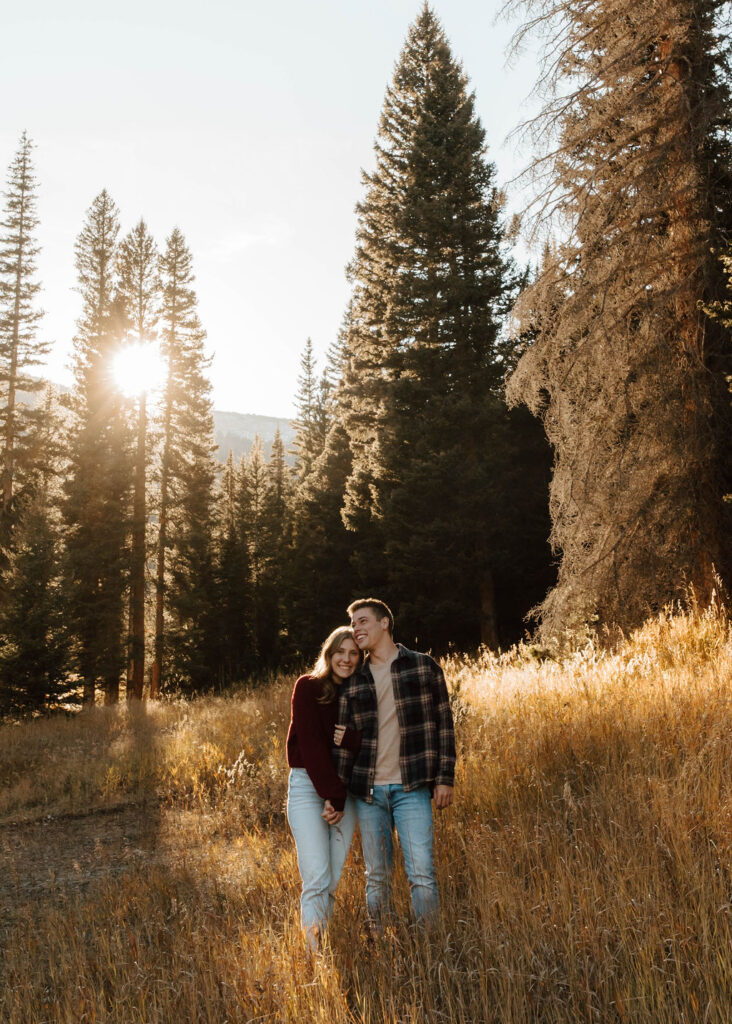 couple stands together in the tall grass with trees behind them