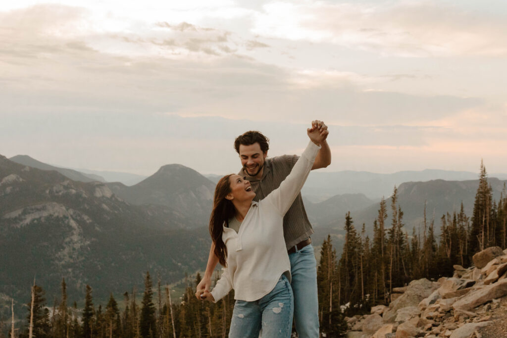 couple holds hands and dances around on top of mountain
