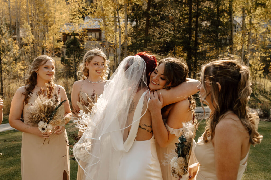 bridesmaids hug bride with smiles on their faces during authentic documentary wedding photos