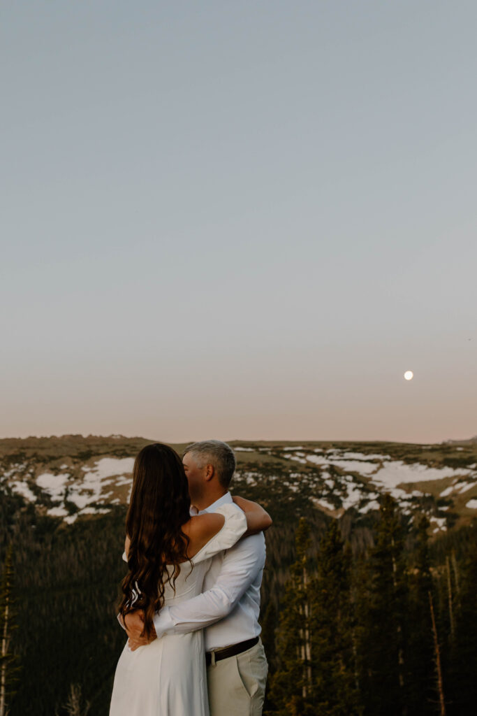 the moon over a couple together in the mountains 